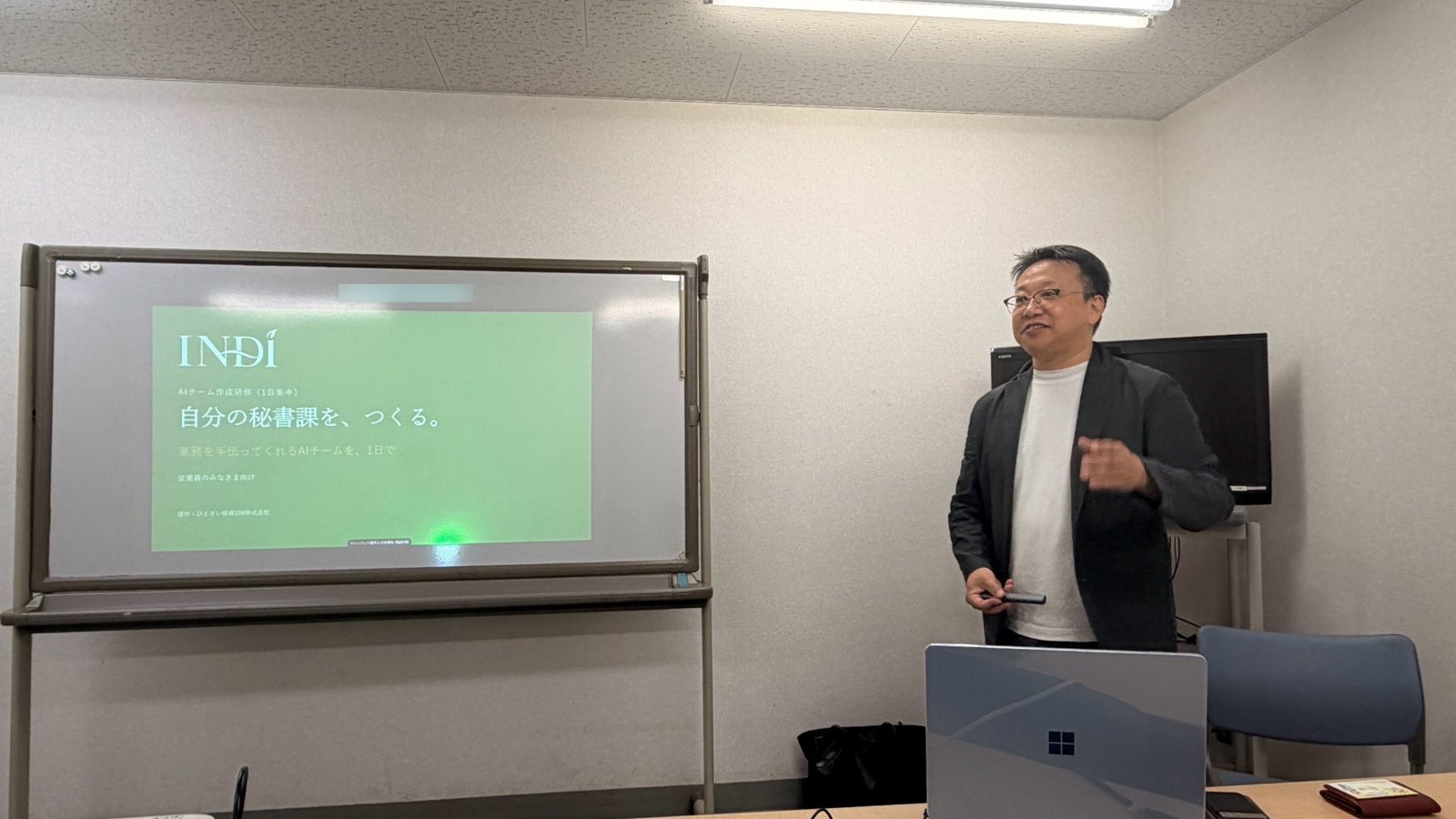 AIチーム作成研修の会場で、代表の岡本が表紙のスライドの前で話している様子